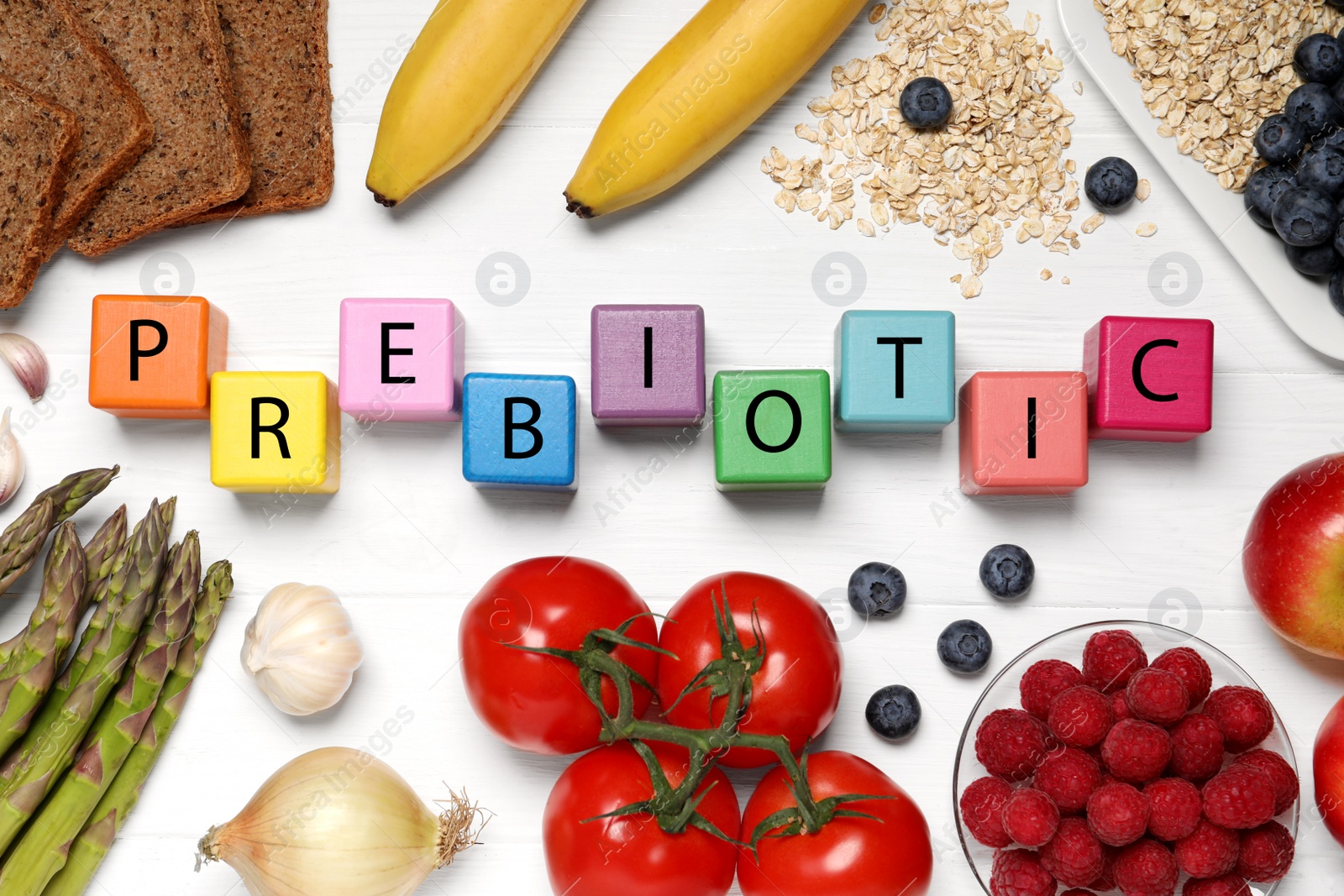 Photo of Word Prebiotic made of cubes with letters and foodstuff on white wooden table, flat lay