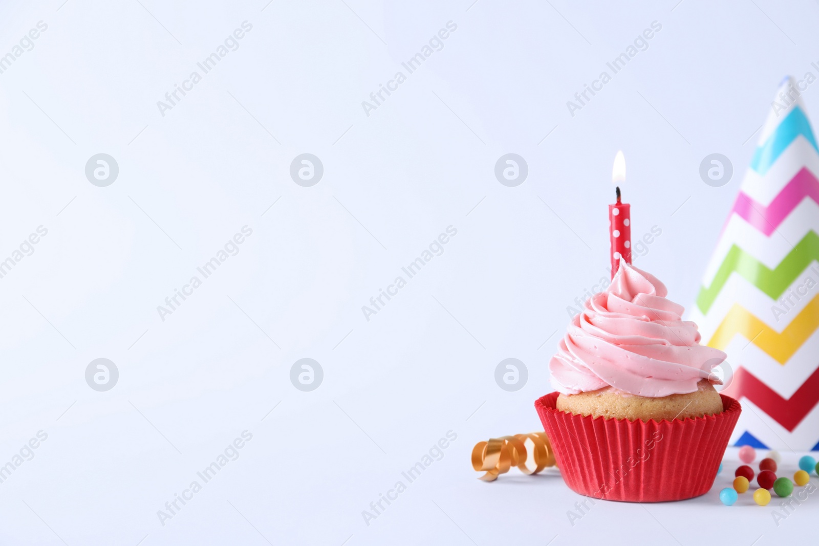 Photo of Delicious birthday cupcake with burning candle, sprinkles and party decor on white background, space for text