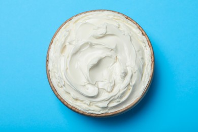 Photo of Bowl of tasty cream cheese on light blue background, top view