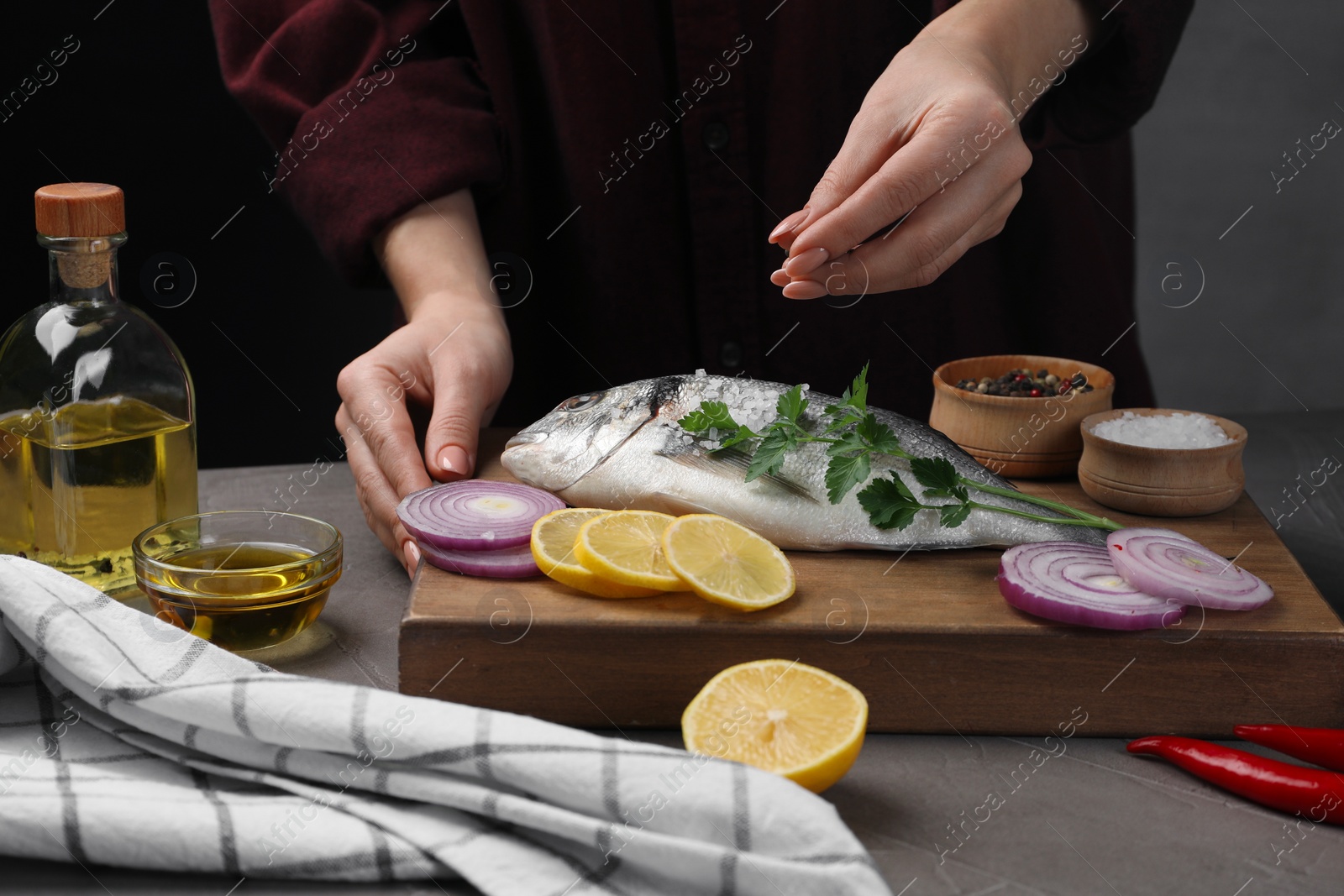 Photo of Woman salting raw dorado fish at grey table, closeup