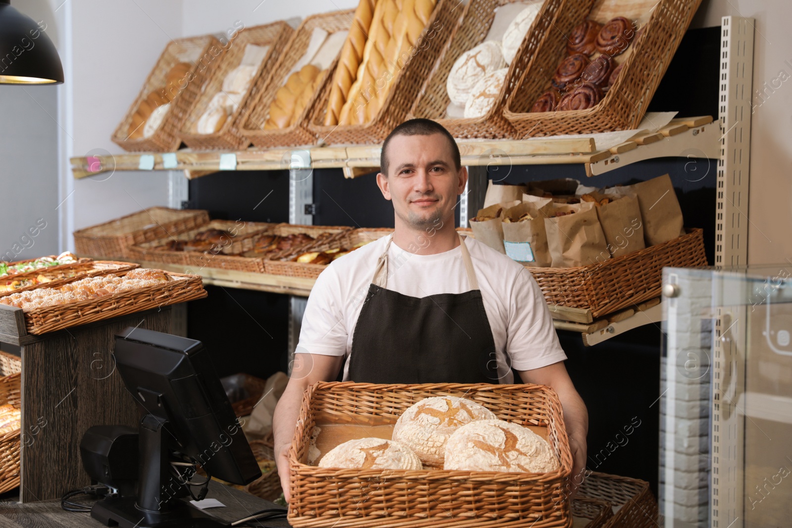 Photo of Portrait of professional baker holding tray with fresh bread near showcase in store