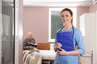 Portrait of nurse with clipboard in senior patient's hospital ward