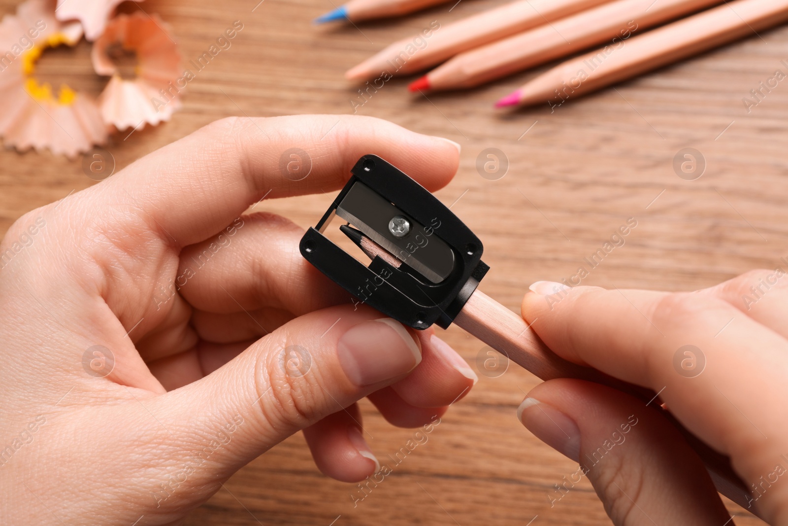 Photo of Woman sharpening pencil at wooden table, closeup