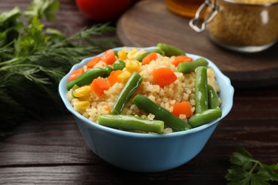 Delicious bulgur with vegetables in bowl on wooden table, closeup