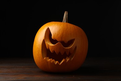 Scary jack o'lantern made of pumpkin on wooden table in darkness. Halloween traditional decor