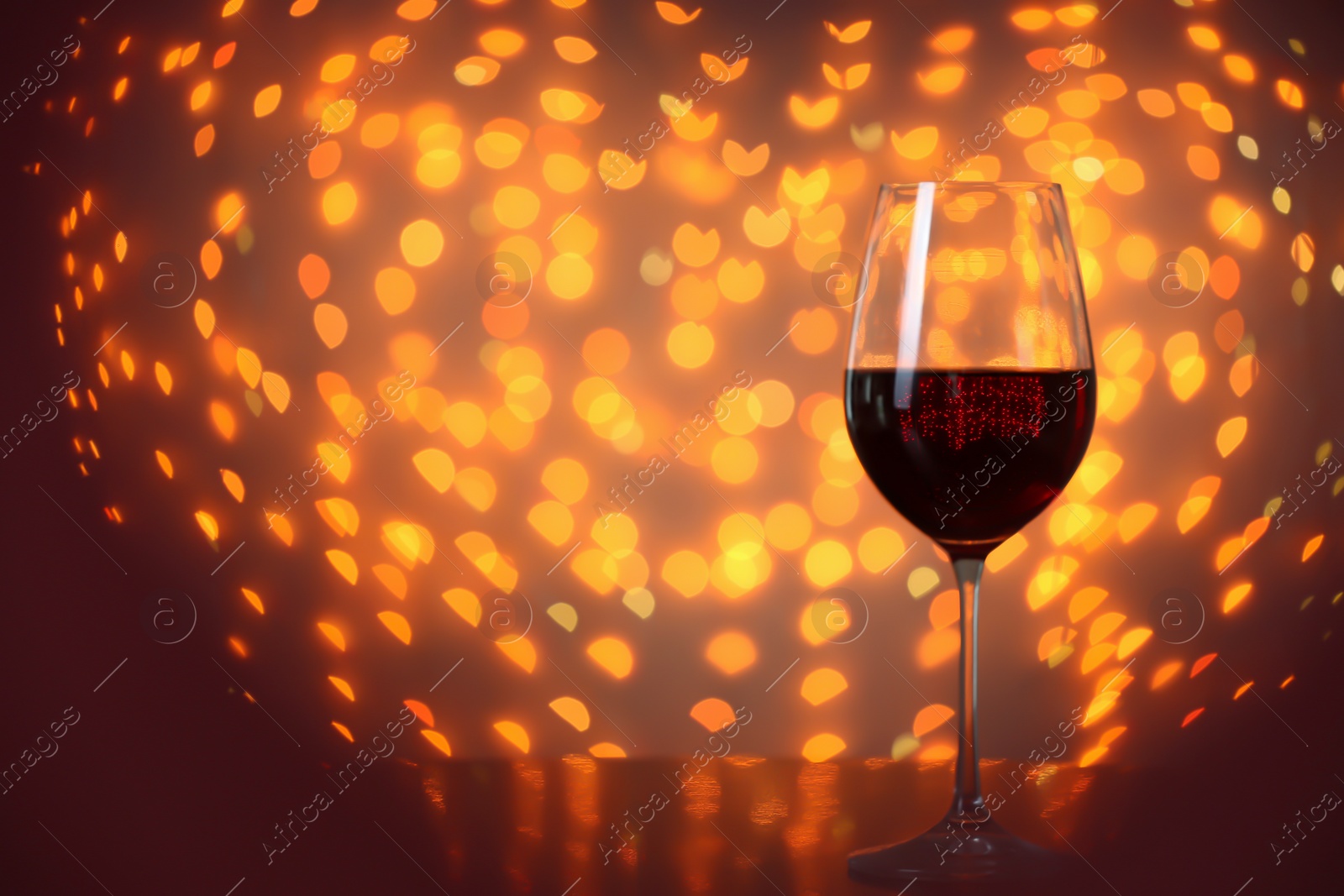 Photo of Glass of wine on table against blurred lights. Space for text