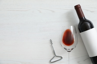 Flat lay composition with bottle of wine and elegant glass on white wooden background. Space for text