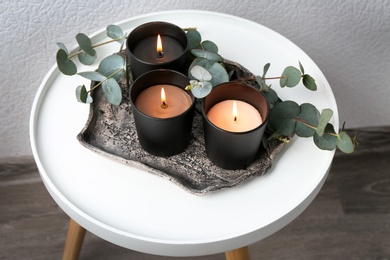 Tray with burning candles and branches on table