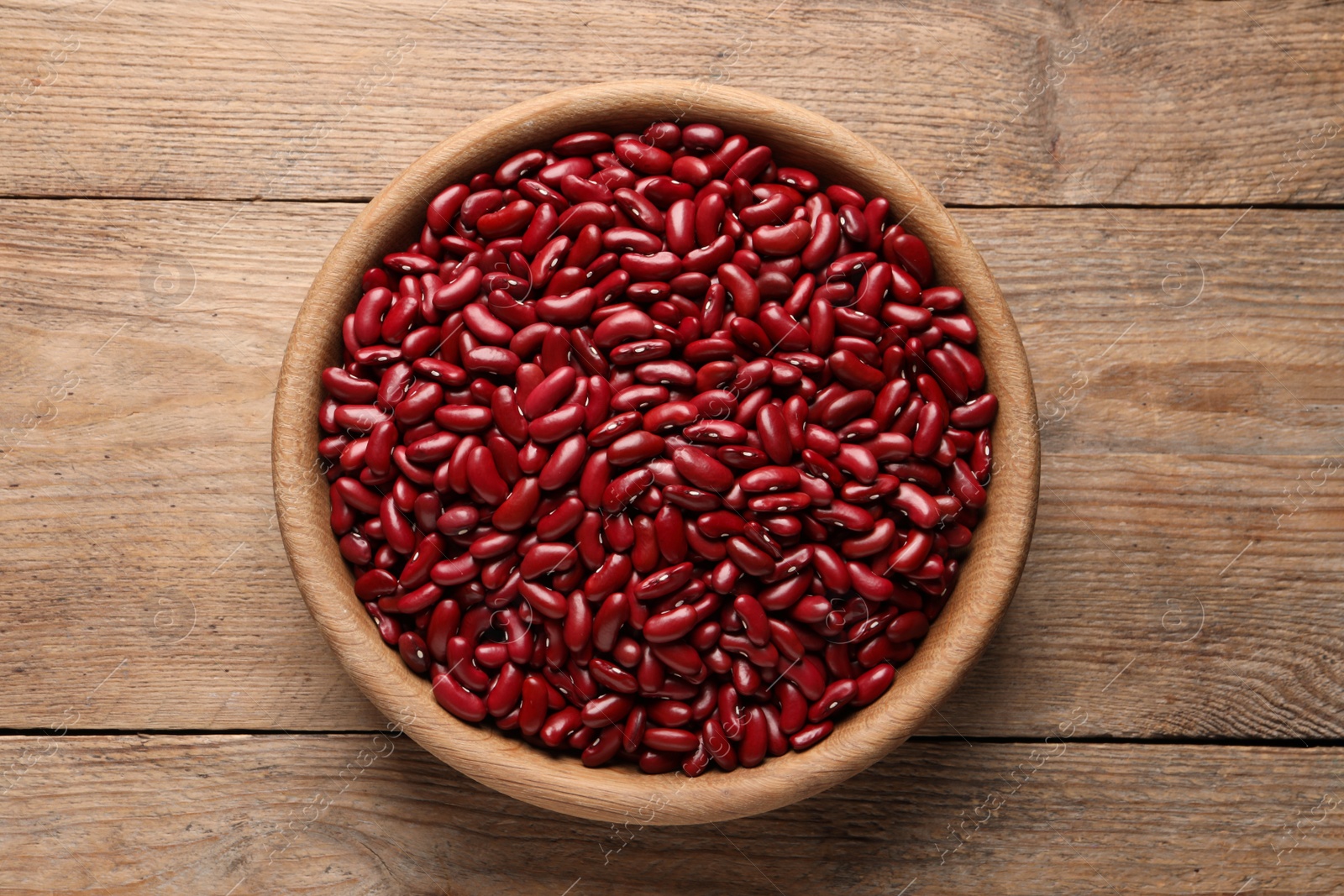 Photo of Raw red kidney beans in bowl on wooden table, top view