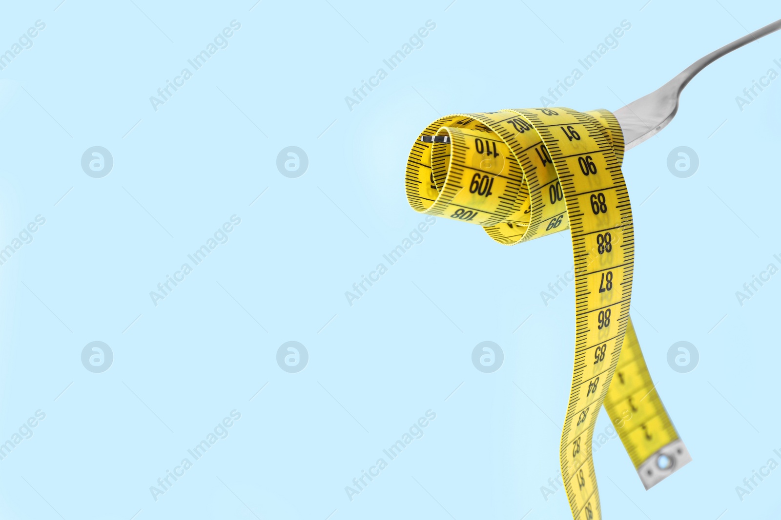 Photo of Fork with measuring tape on light blue background, space for text. Diet concept