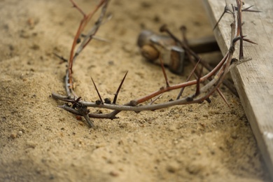 Photo of Crown of thorns, wooden plank and hammer with nails on sand. Easter attributes