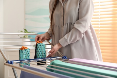 Young woman hanging clean laundry on drying rack at home, closeup