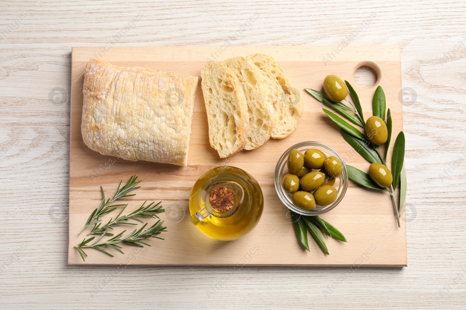 Photo of Cooking oil in jug, olives, rosemary and ciabatta bread on wooden table, flat lay