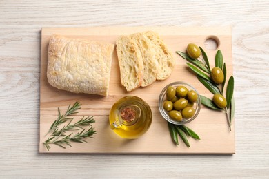 Photo of Cooking oil in jug, olives, rosemary and ciabatta bread on wooden table, flat lay