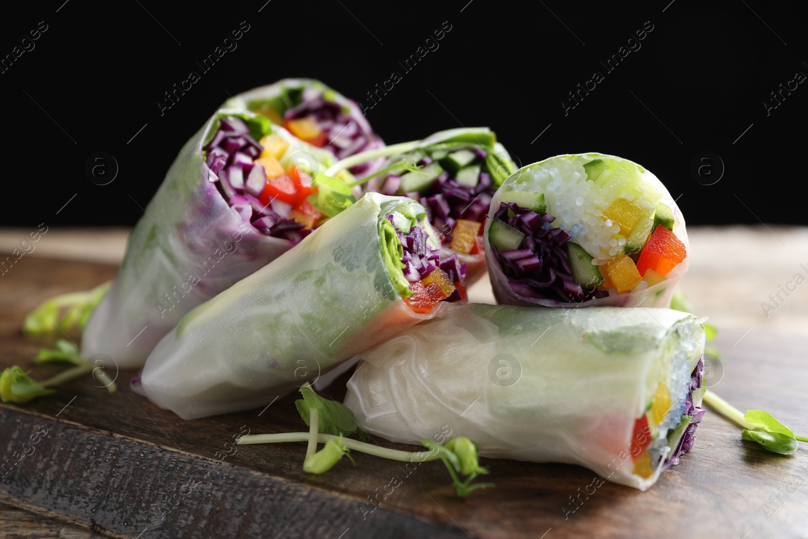 Photo of Delicious spring rolls wrapped in rice paper on wooden board, closeup