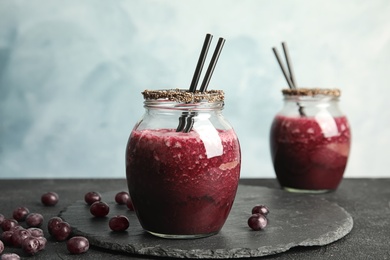 Photo of Jar of delicious acai juice with cocktail straws on dark table against blurred background