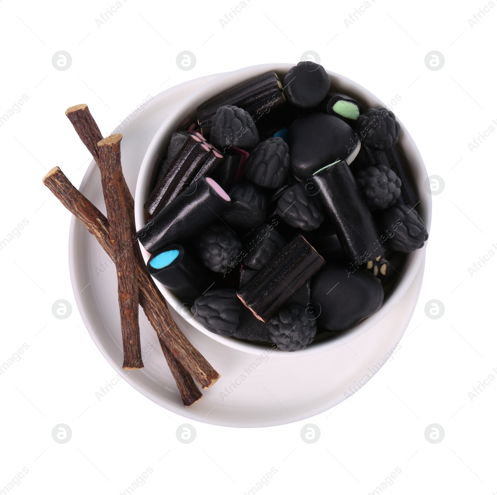 Photo of Bowl with many tasty candies and dried sticks of liquorice root isolated on white, top view