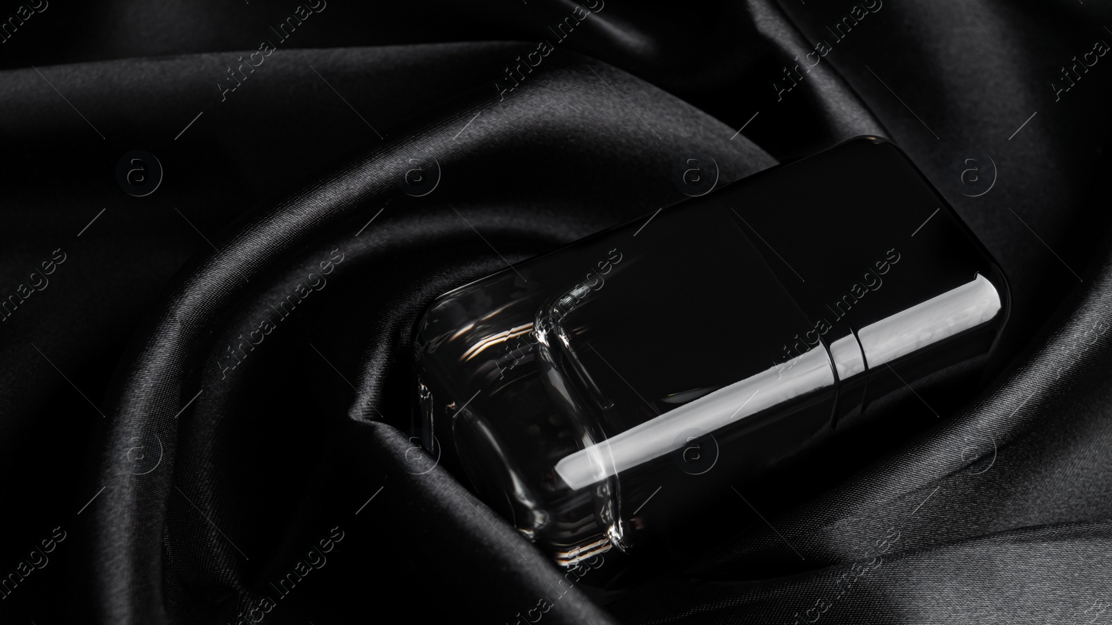 Photo of Luxury bottle of perfume on black silk, closeup