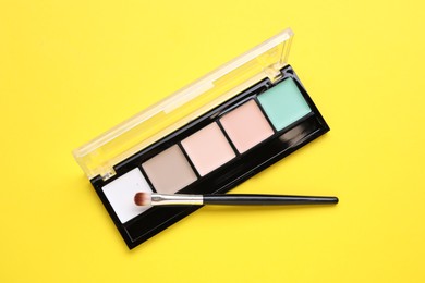 Colorful contouring palette with brush on yellow background, top view. Professional cosmetic product