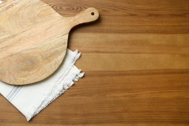 Photo of Empty wooden board and napkin on table, top view. Space for text