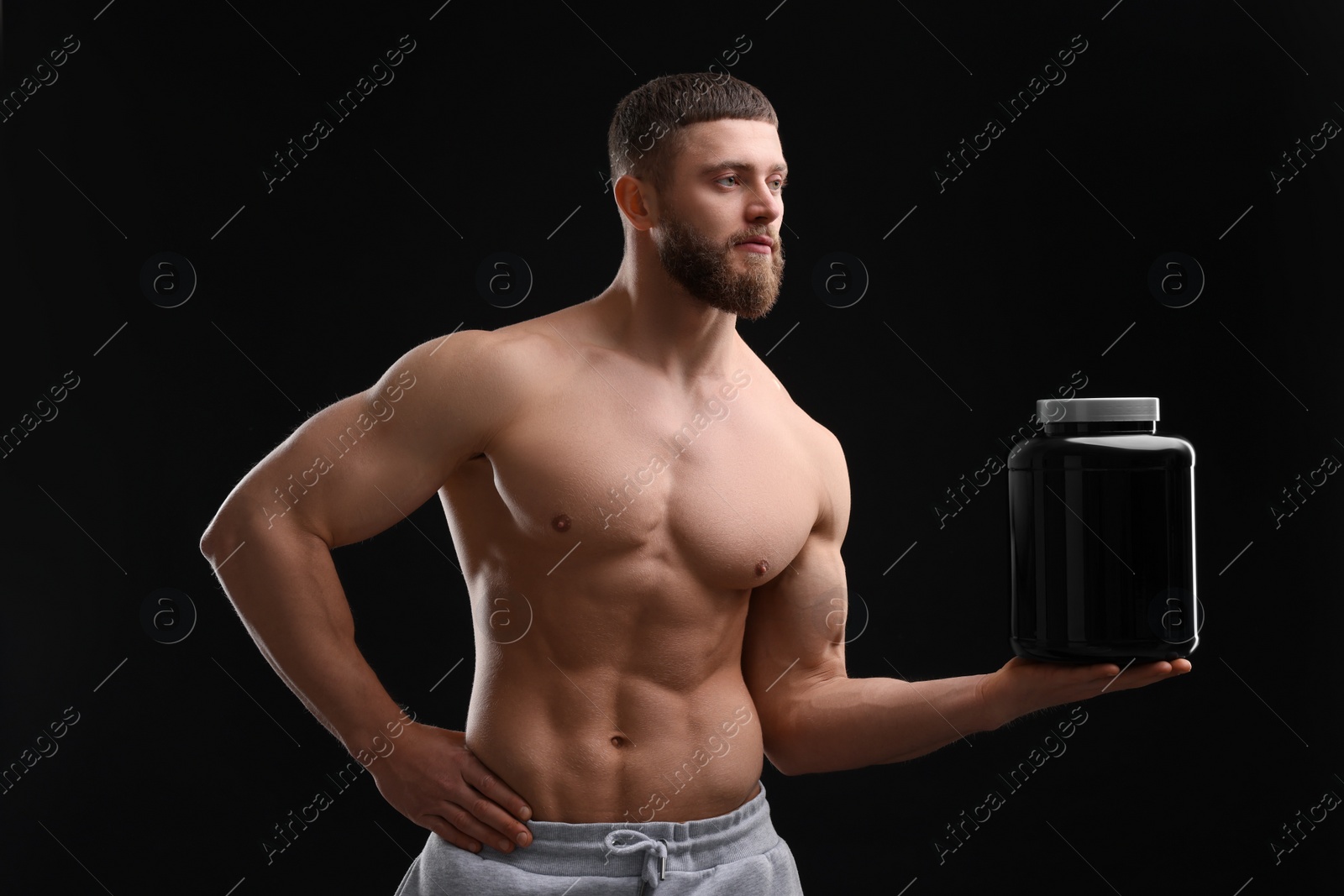 Photo of Young man with muscular body holding jar of protein powder on black background