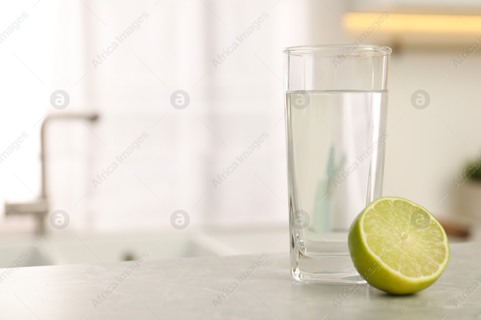 Photo of Filtered water in glass and lime on light table in kitchen, closeup. Space for text