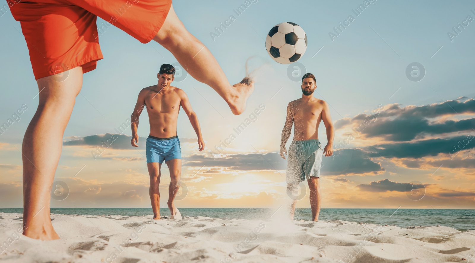 Image of Friends playing football on beach during sunset, low angle view