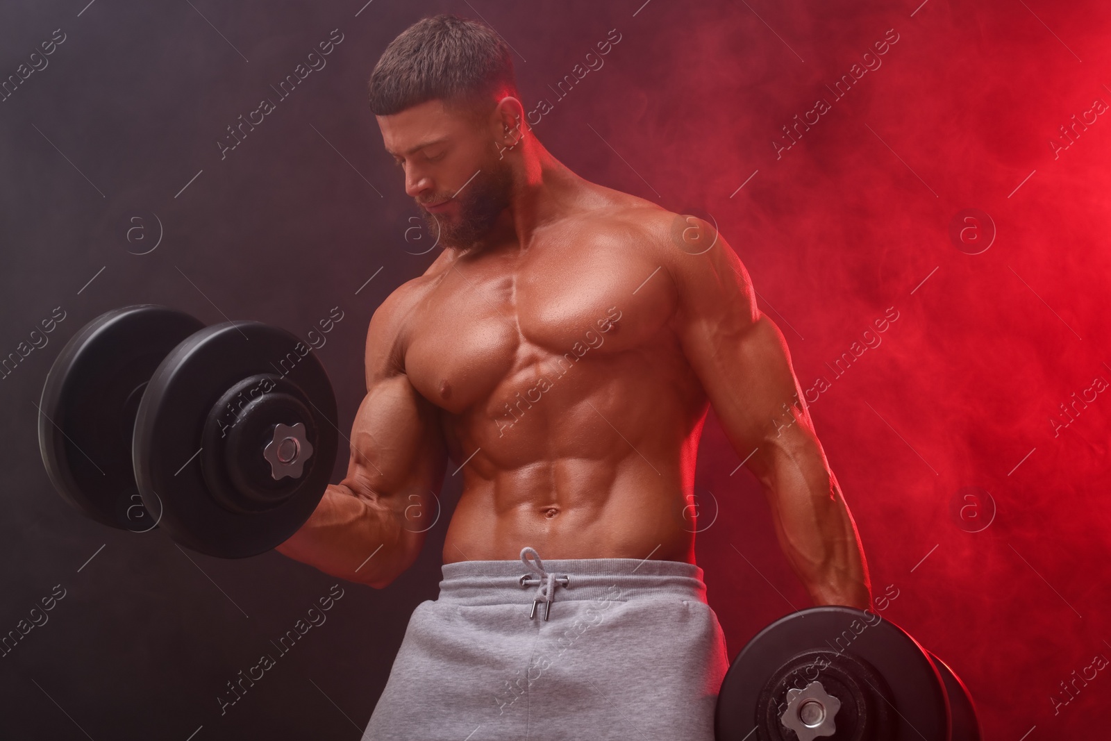 Photo of Young bodybuilder exercising with dumbbells in smoke on color background, low angle view