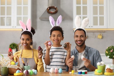 Photo of Happy African American family with Easter eggs at table in kitchen