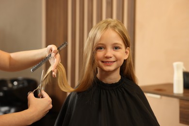 Professional hairdresser cutting girl's hair in beauty salon