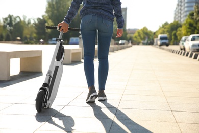 Photo of Woman carrying folded electric kick scooter outdoors. Space for text