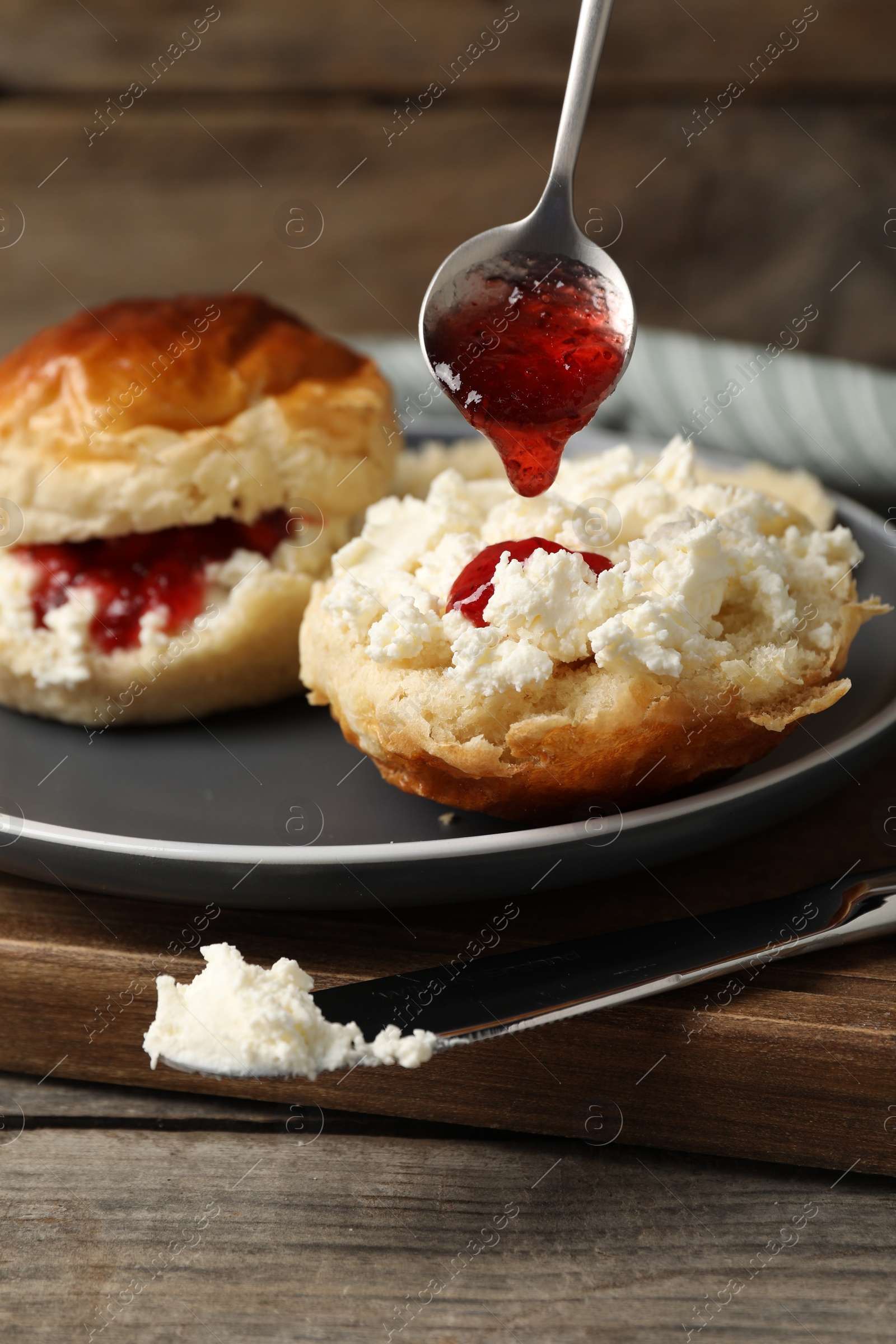 Photo of Pouring cranberry jam from spoon into freshly baked soda water scone on wooden table
