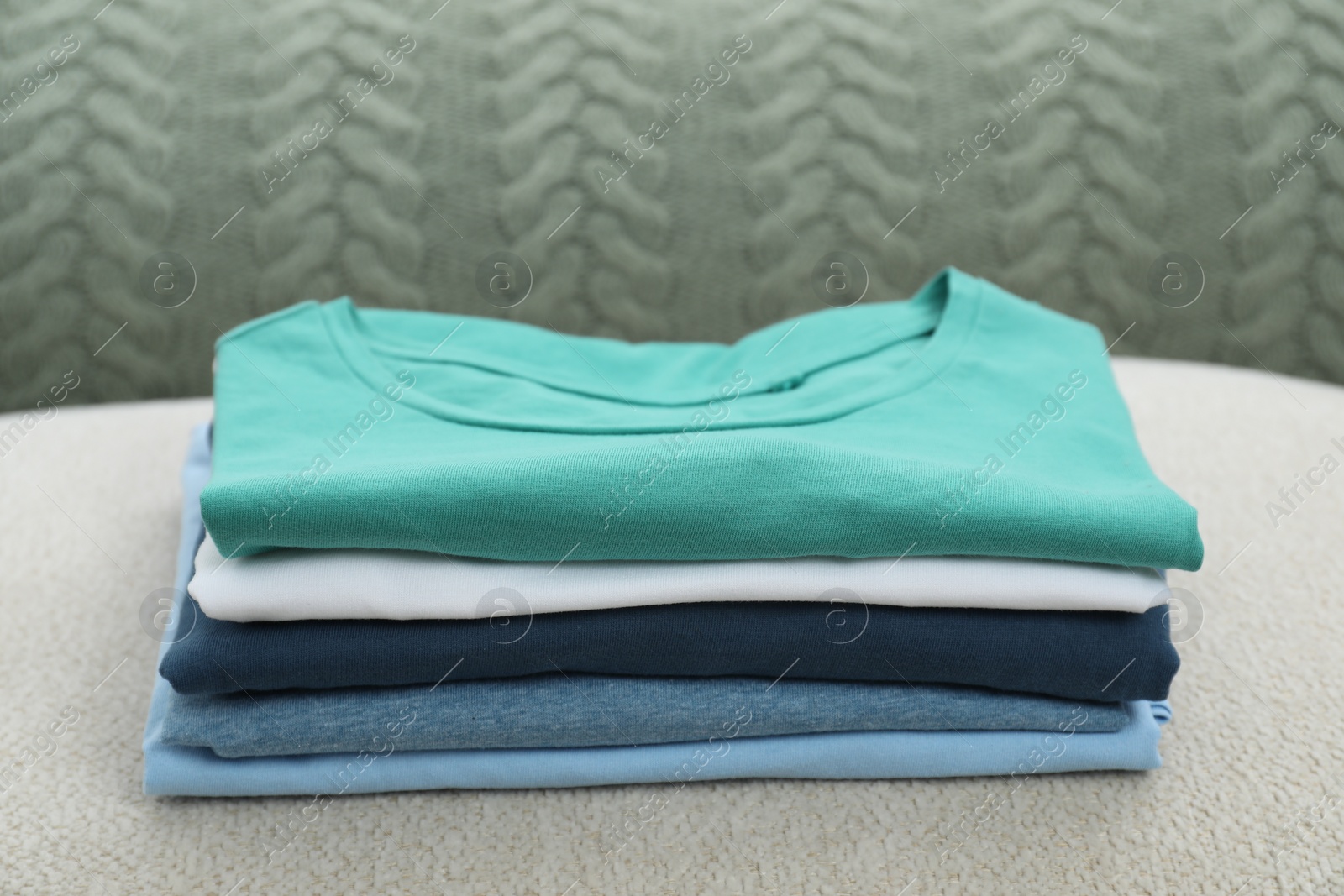 Photo of Sorting and organizing. Stack of different folded clothes on ottoman indoors