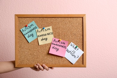 Woman holding board with autism related phrases on color background