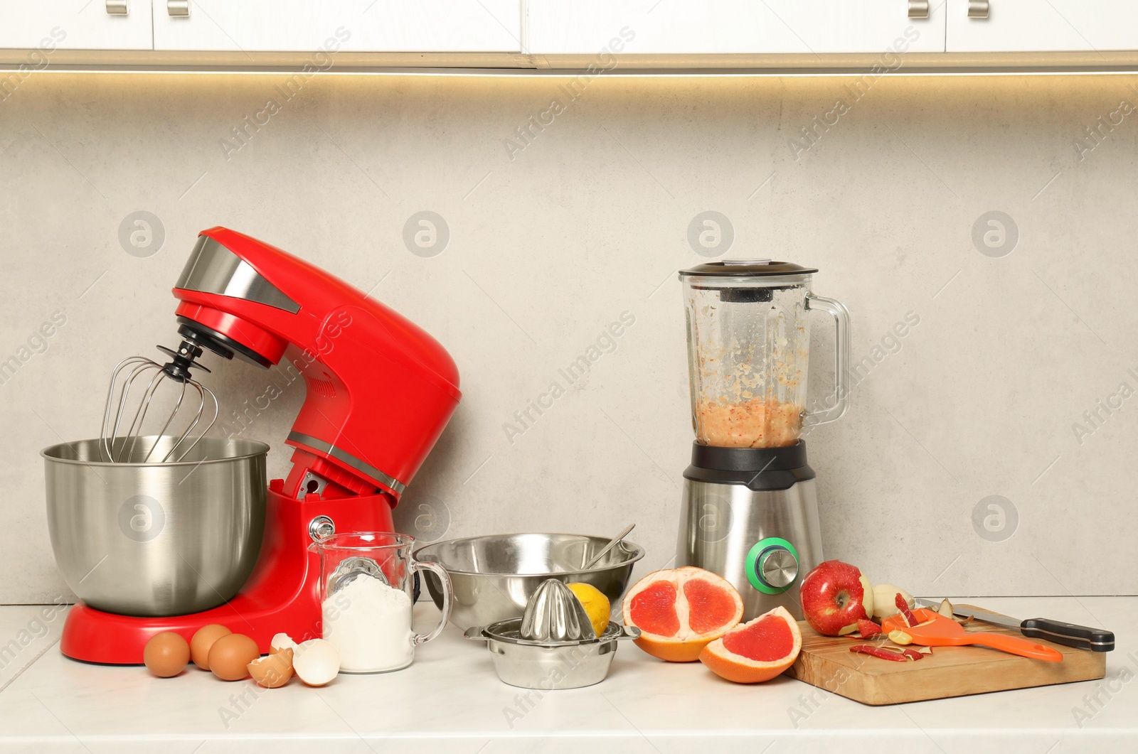 Photo of Modern red stand mixer, blender and different ingredients on white marble countertop in kitchen