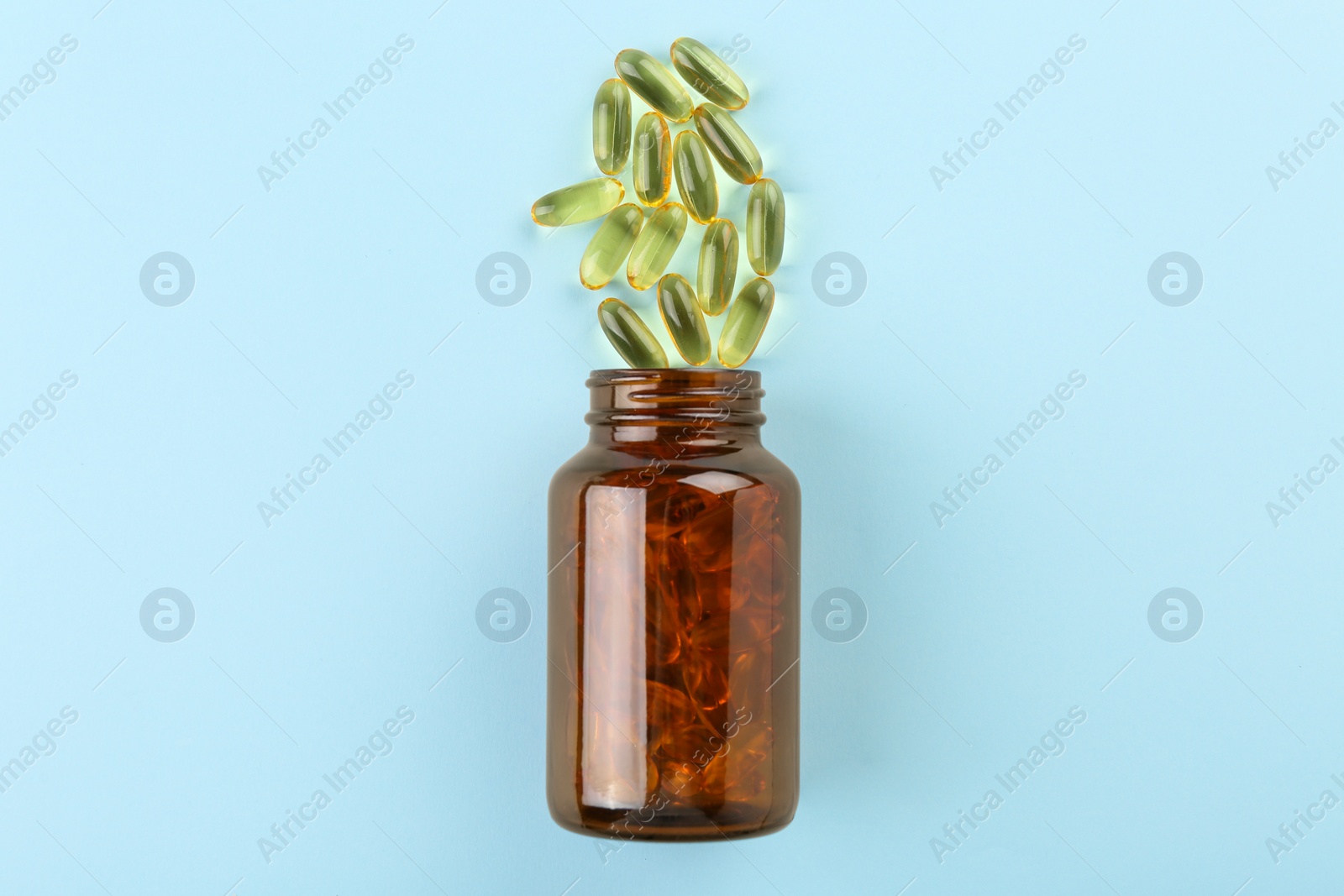 Photo of Bottle and vitamin capsules on light blue background, top view