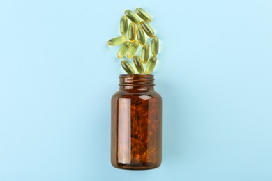 Photo of Bottle and vitamin capsules on light blue background, top view