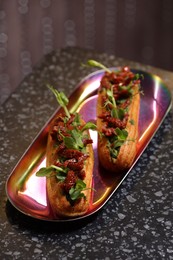 Photo of Tasty eclairs with sun-dried tomatoes and microgreens on dark table