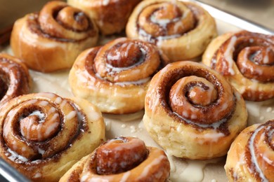 Photo of Tasty cinnamon rolls with cream on parchment paper, closeup