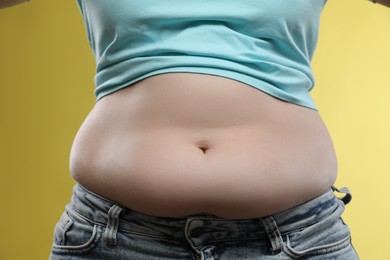 Photo of Woman with excessive belly fat on yellow background, closeup. Overweight problem