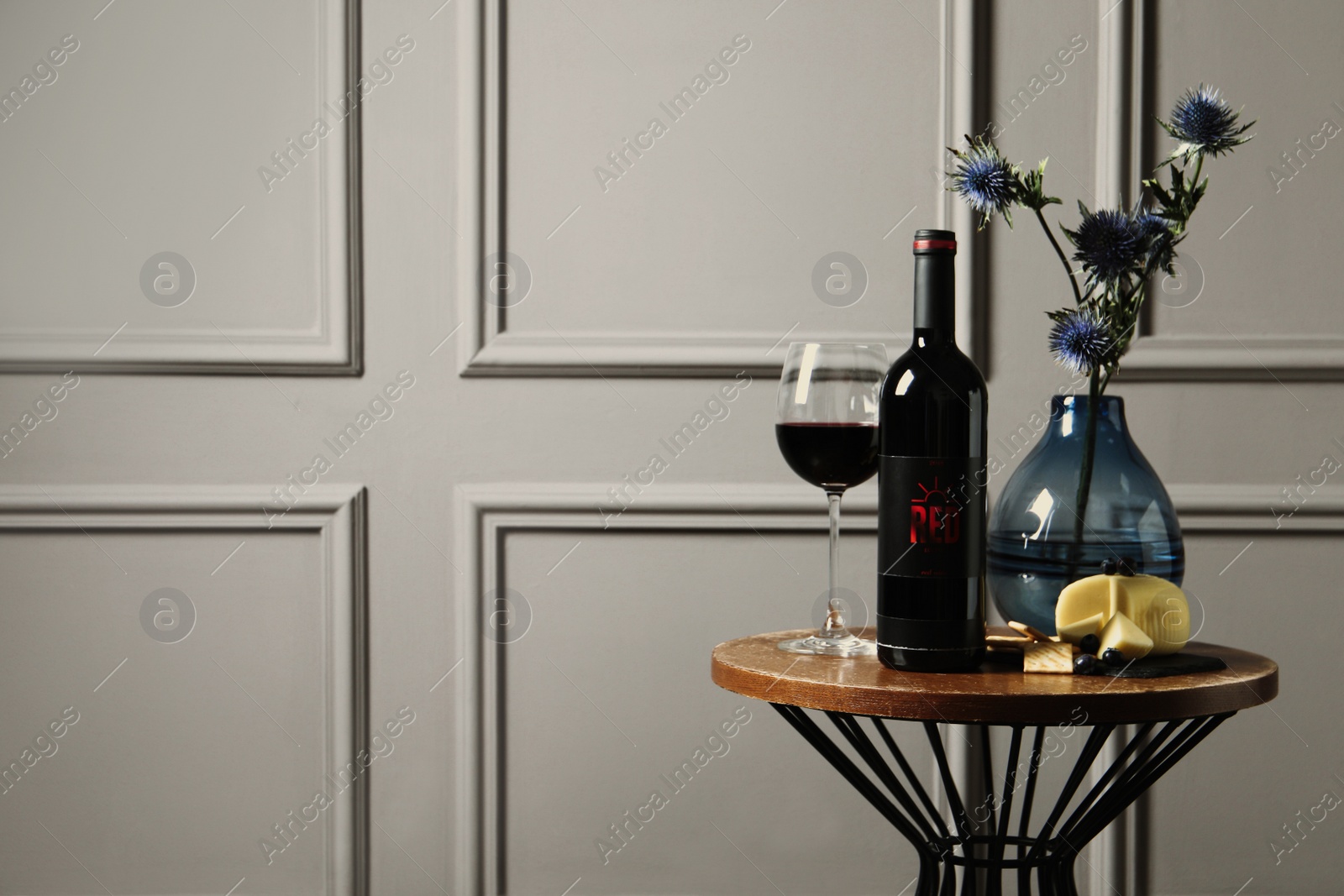 Photo of Bottle of red wine, glass, delicious snacks and beautiful bouquet on wooden table indoors. Space for text