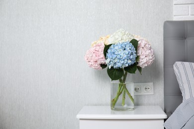 Photo of Beautiful hydrangea flowers in vase on white bedside table indoors, space for text