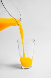 Photo of Pouring fresh orange juice into glass on white background