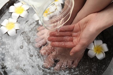 Woman pouring water onto hand while soaking her feet in bowl, above view. Spa treatment