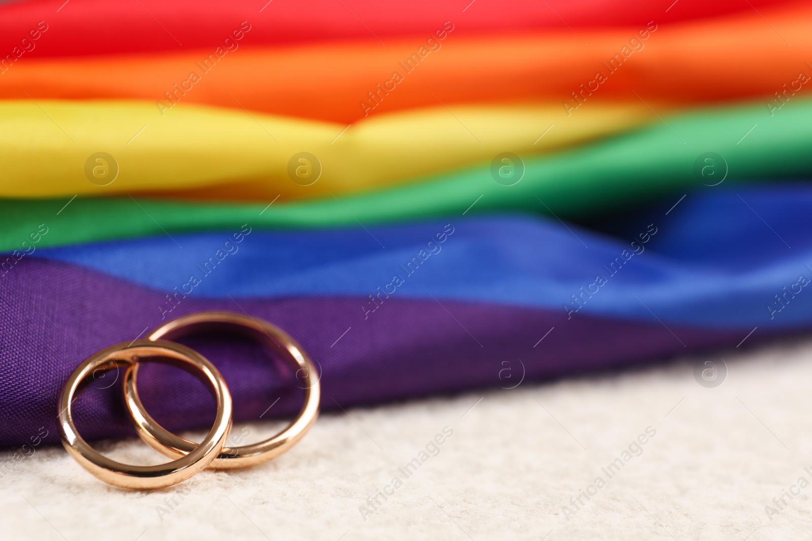 Photo of Rainbow LGBT flag and wedding rings on white background, closeup