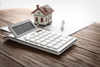 Photo of Calculator, house model, pen and documents on wooden table. Real estate agent's workplace