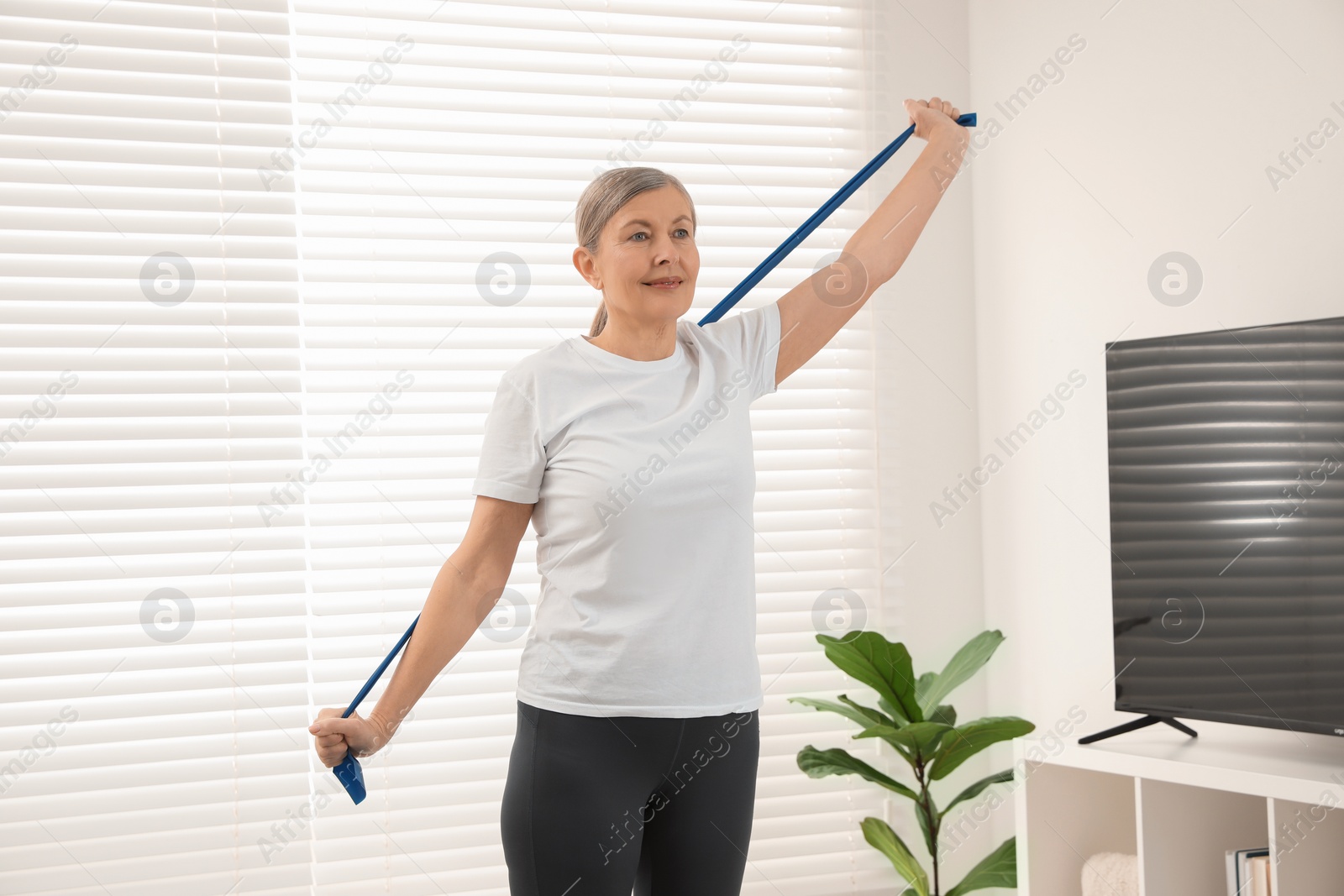 Photo of Senior woman doing exercise with fitness elastic band at home