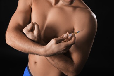 Athletic man injecting himself on black background, closeup. Doping concept
