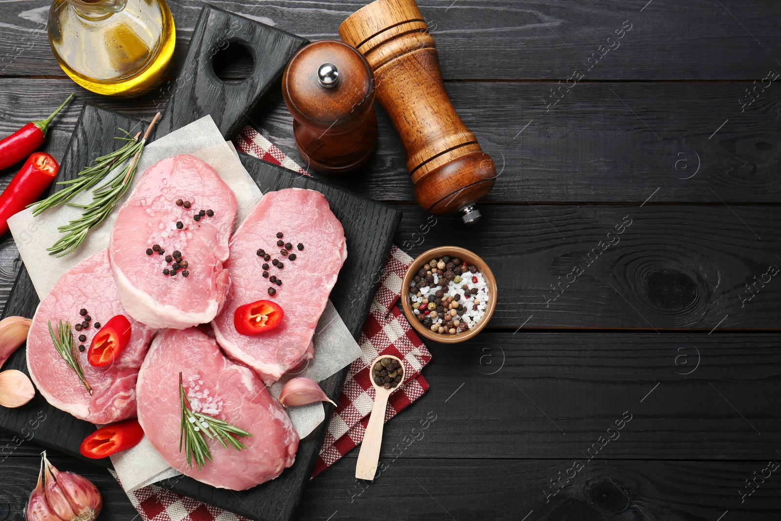 Photo of Pieces of raw pork meat, chili peppers and spices on black wooden table, flat lay. Space for text