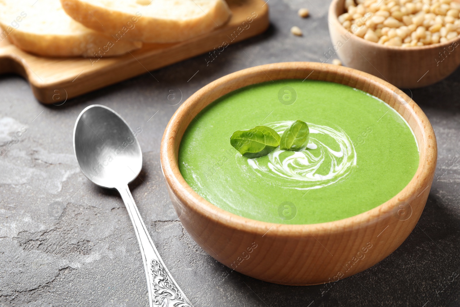 Photo of Bowl of healthy green soup with fresh spinach on grey table